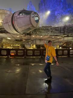Person in t-shirt and pants standing in front of a spaceship from the Star Wars movies after dark